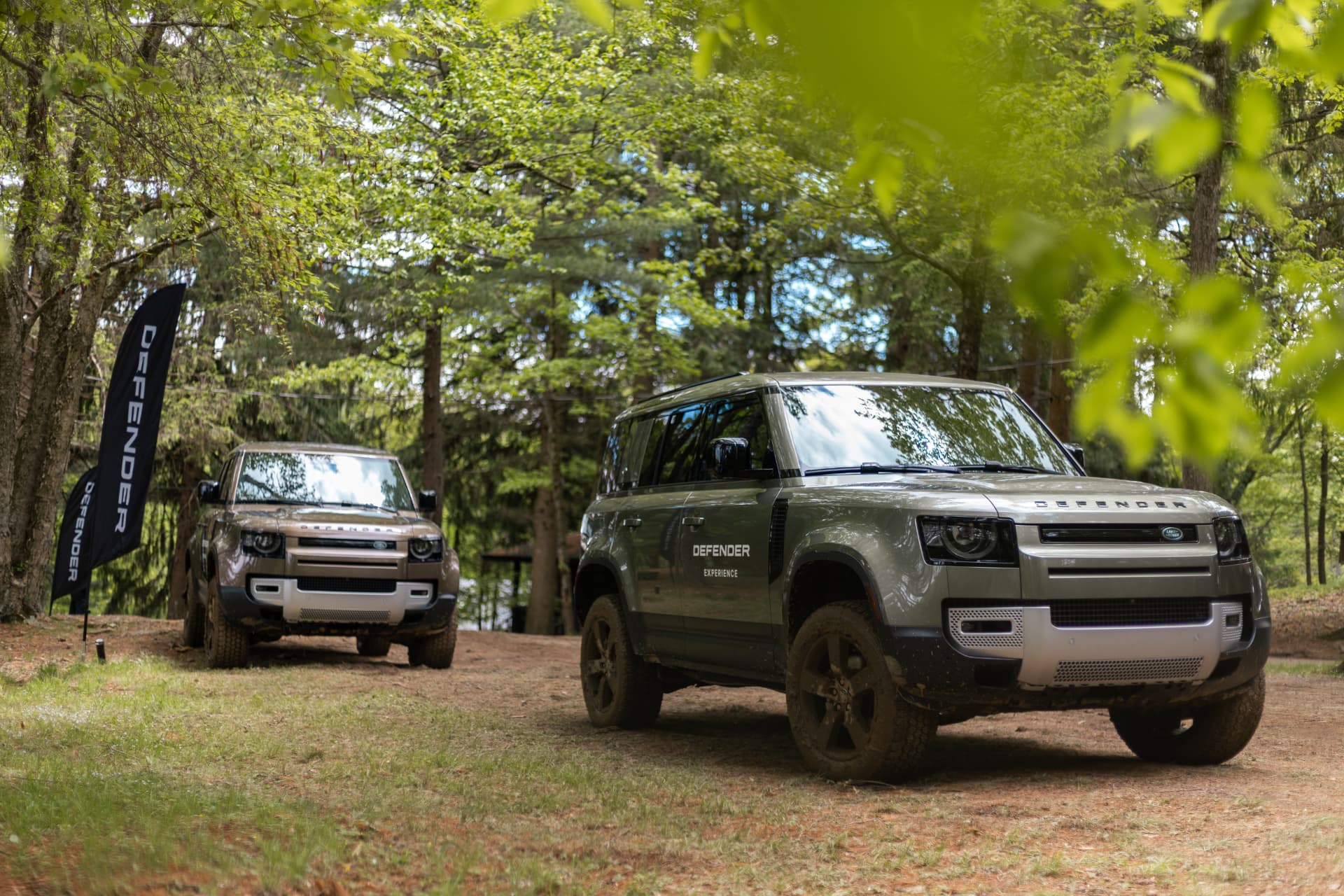 Two Land Rover Defenders parked on a forest track at a Defender Experience event