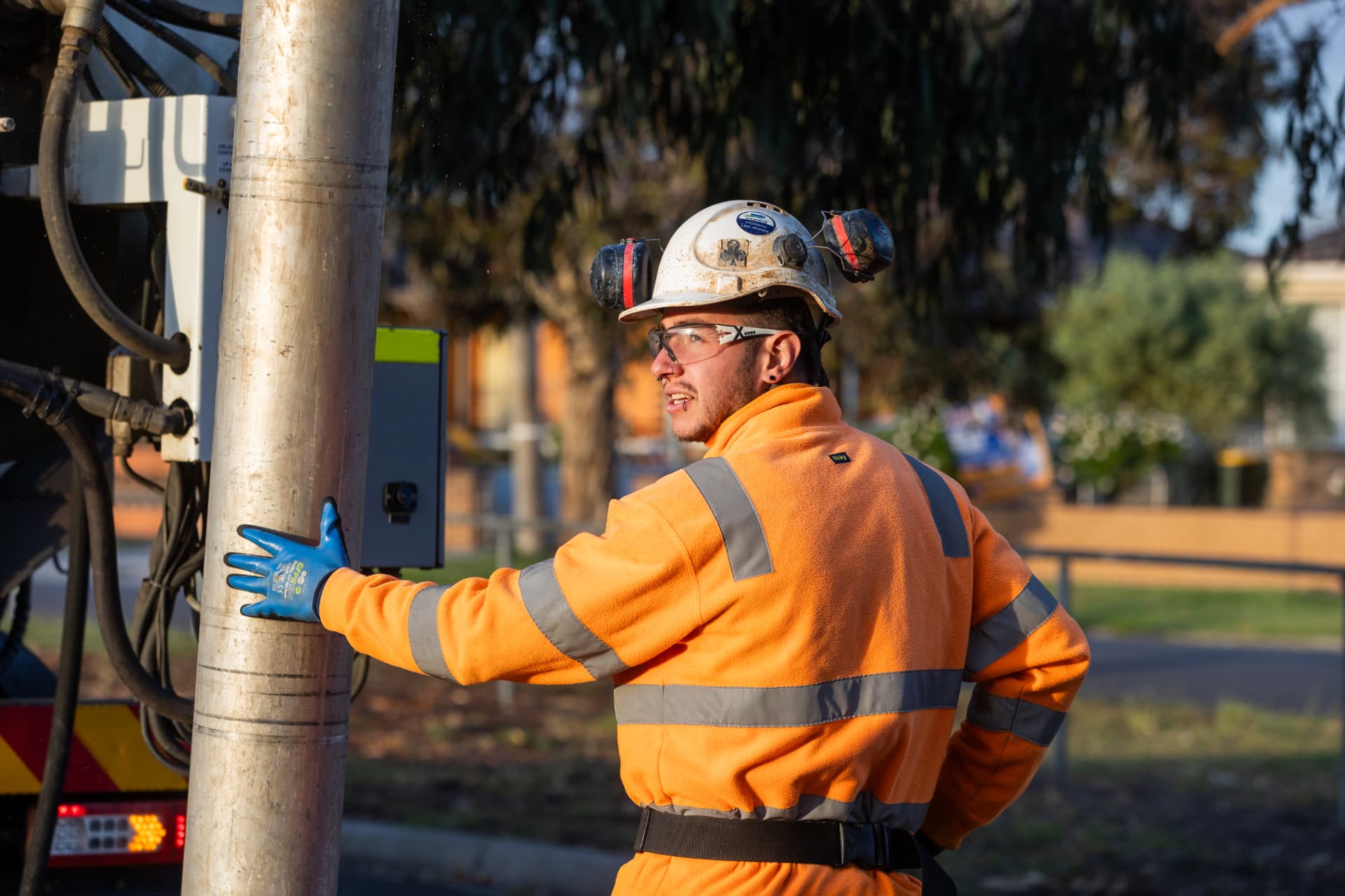 Worker in hi-vis orange clothing and hard hat next to drilling equipment